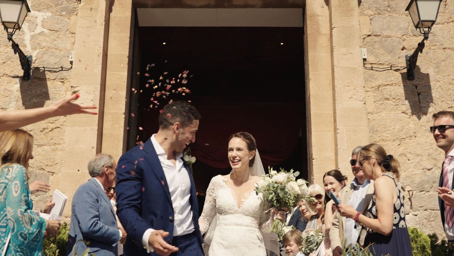 Newlyweds leaving the church as guests celebrate them with petals and confetti.