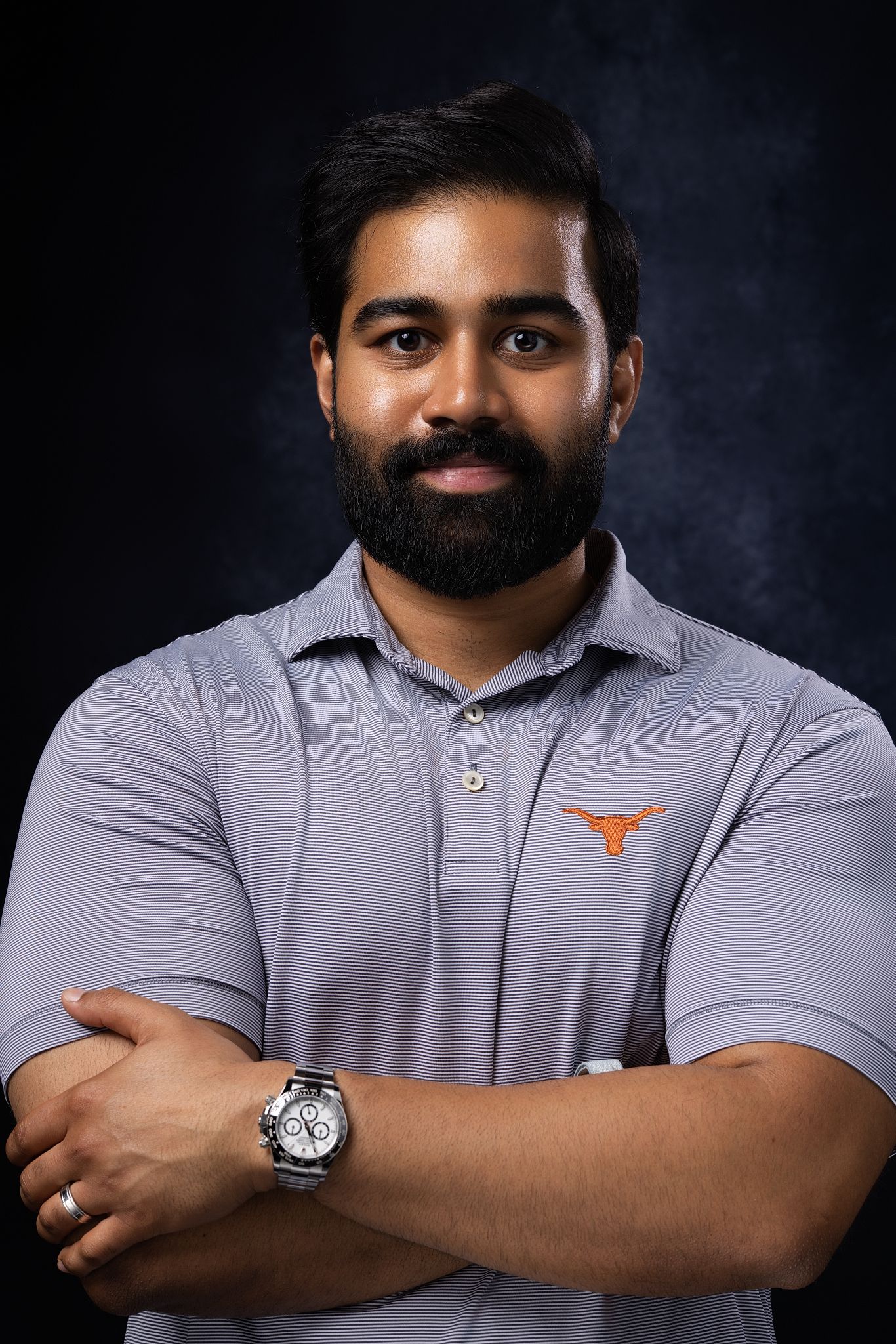 Young bearded man in gray University of Texas Longhorns polo shirt with arms crossed wearing a silver watch.