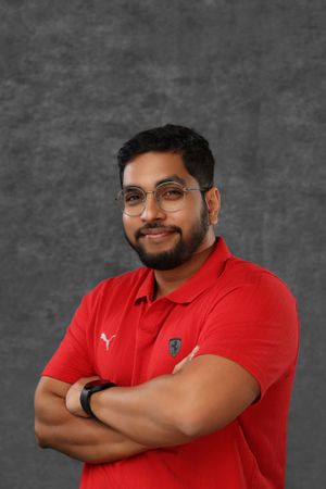 Smiling man with beard and glasses in a red Puma Ferrari polo shirt with arms crossed on gray background.