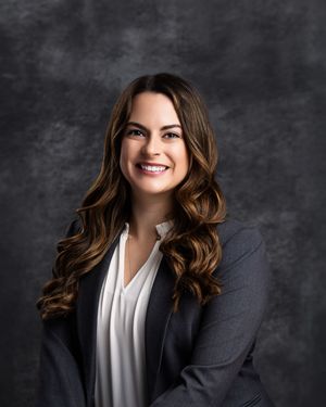 Smiling brunette woman in navy blazer poses with arms crossed for professional headshot.
