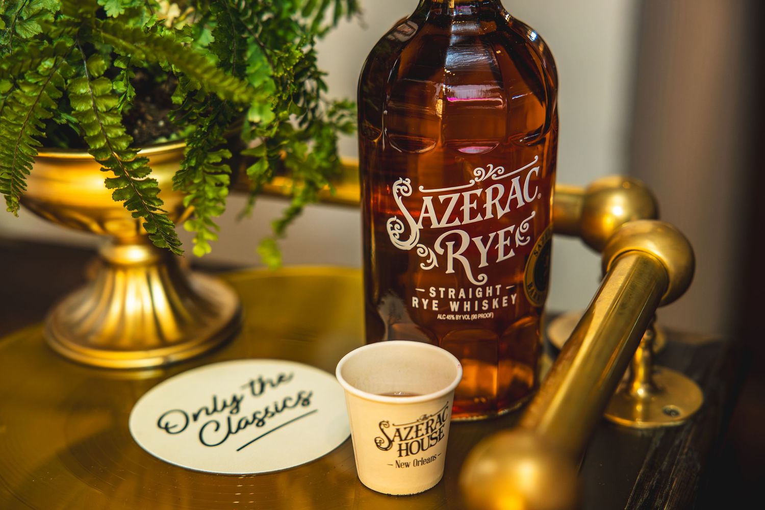 Sazerac Rye whiskey bottle displayed with gold decor and ferns in elegant setting.