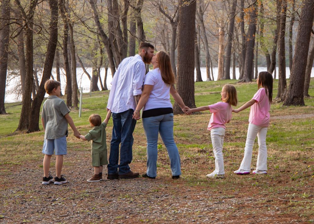 Family of five enjoying an autumn walk together in a peaceful wooded park area near the water.