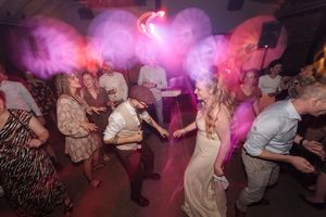 Wedding reception dance floor filled with guests under vibrant purple lighting.