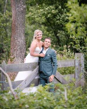 Couple sharing romantic moments on a rustic wooden fence surrounded by lush greenery.