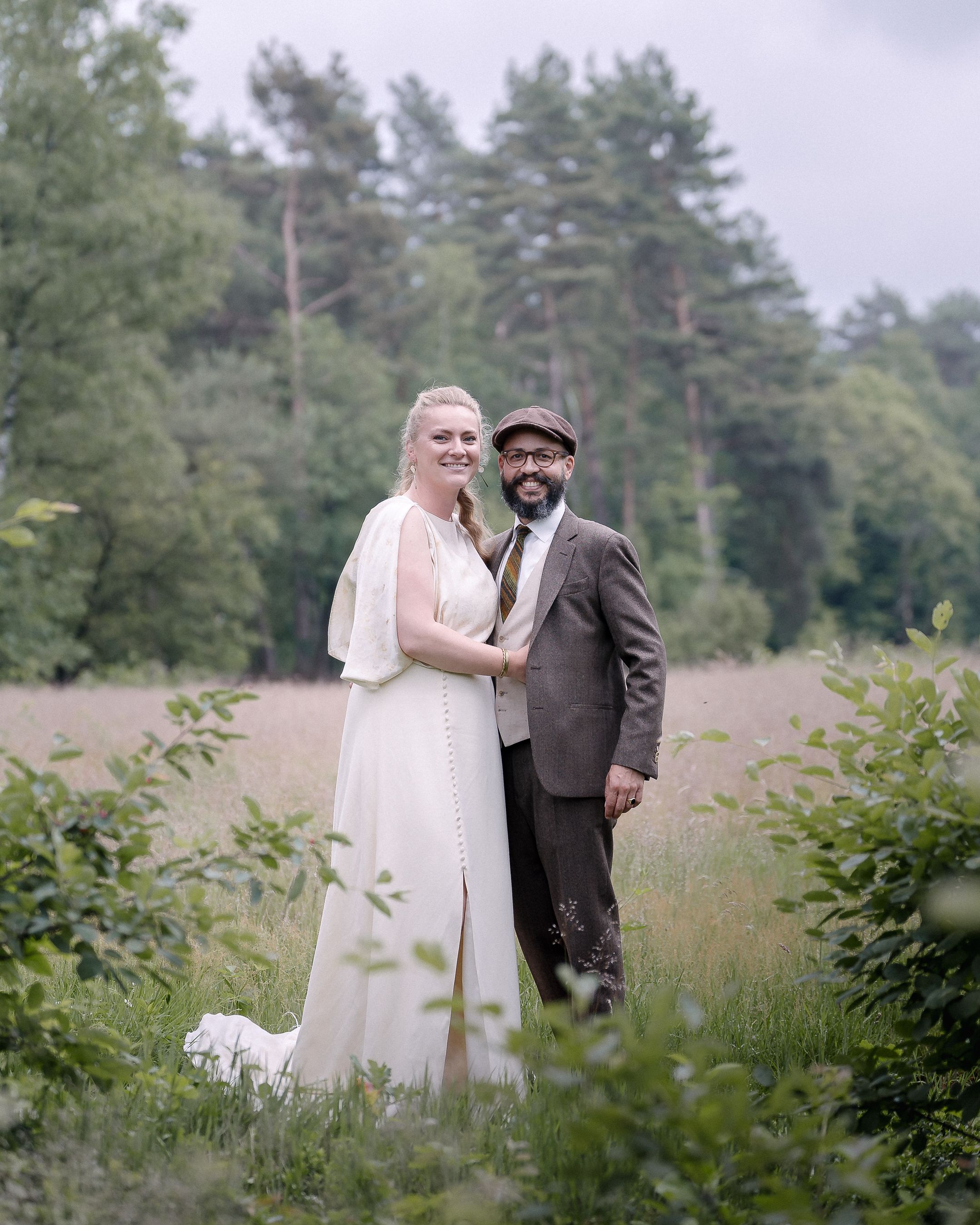 A couple shares intimate moments in a meadow surrounded by tall grasses and pine trees.