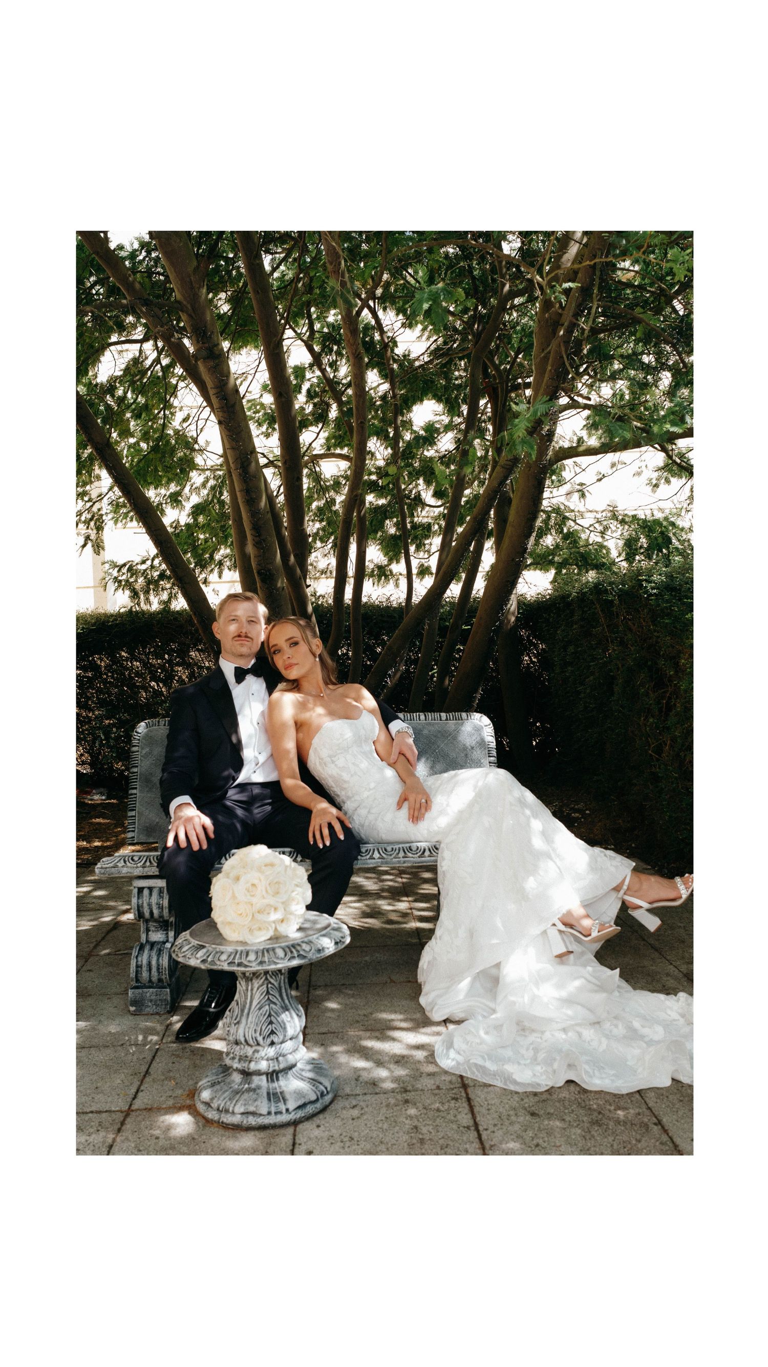 A bride and groom share romantic poses on an elegant ice sculpture bench in an outdoor garden setting.