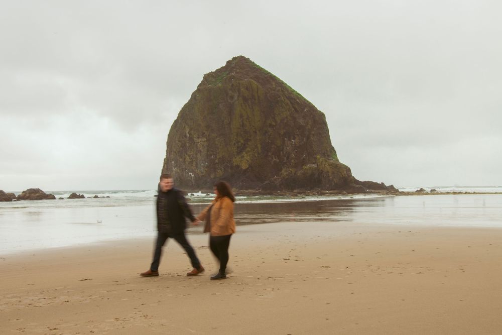 People walking on beach near Haystack Rock at Cannon Beach, Oregon under cloudy skies.