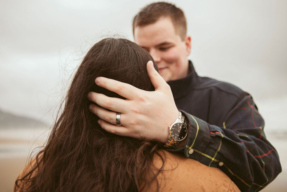 A couple embraces intimately outdoors with soft lighting as the person in dark clothing holds their partner close.
