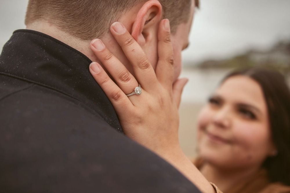 Close-up shot of a couple's engagement moment showing a diamond ring and tender embrace.