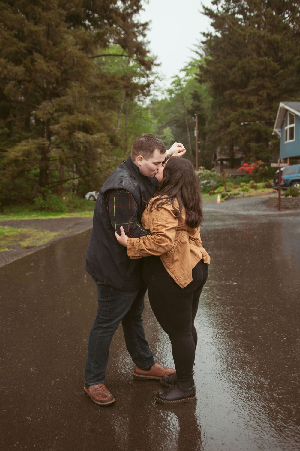 A sequence of people engaging in a playful dance movement on a wet road surrounded by evergreen trees.
