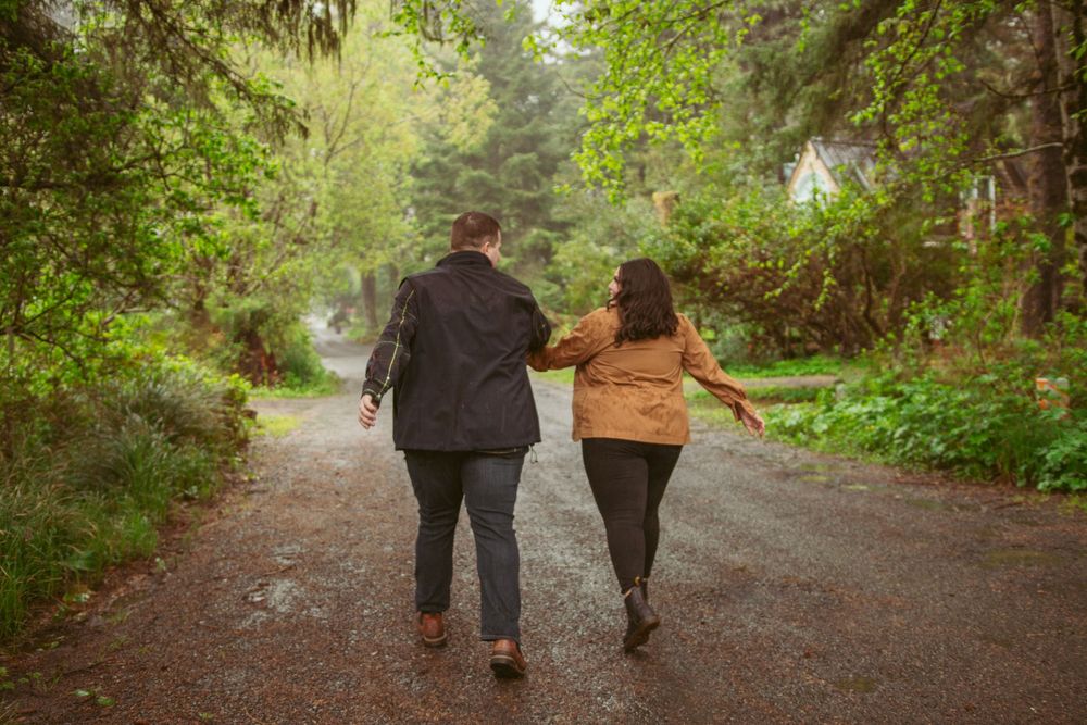 Couple walking together down a scenic forest path surrounded by lush green foliage on a misty day.