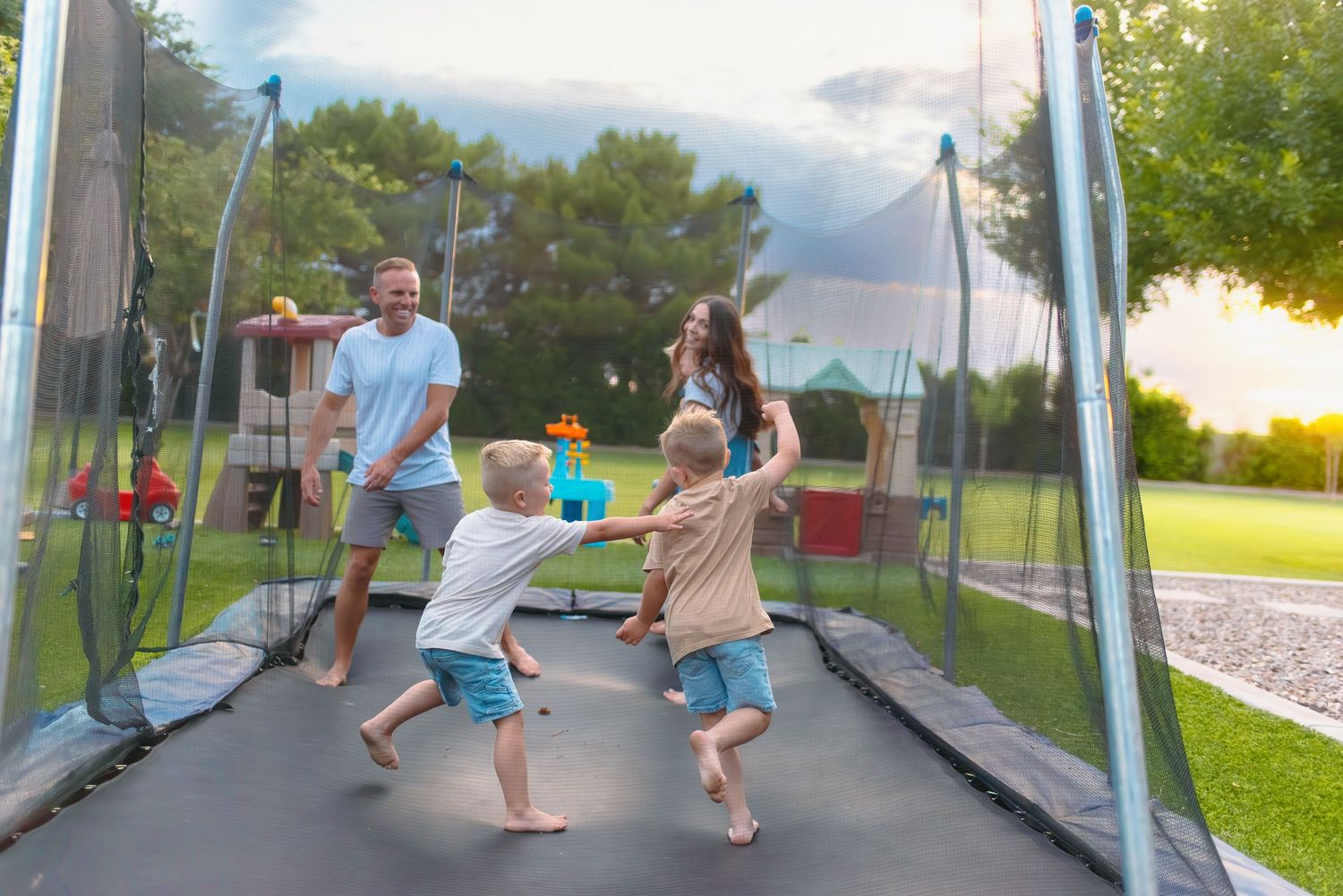 Family enjoying outdoor fun together jumping on a backyard trampoline during a sunny summer evening.