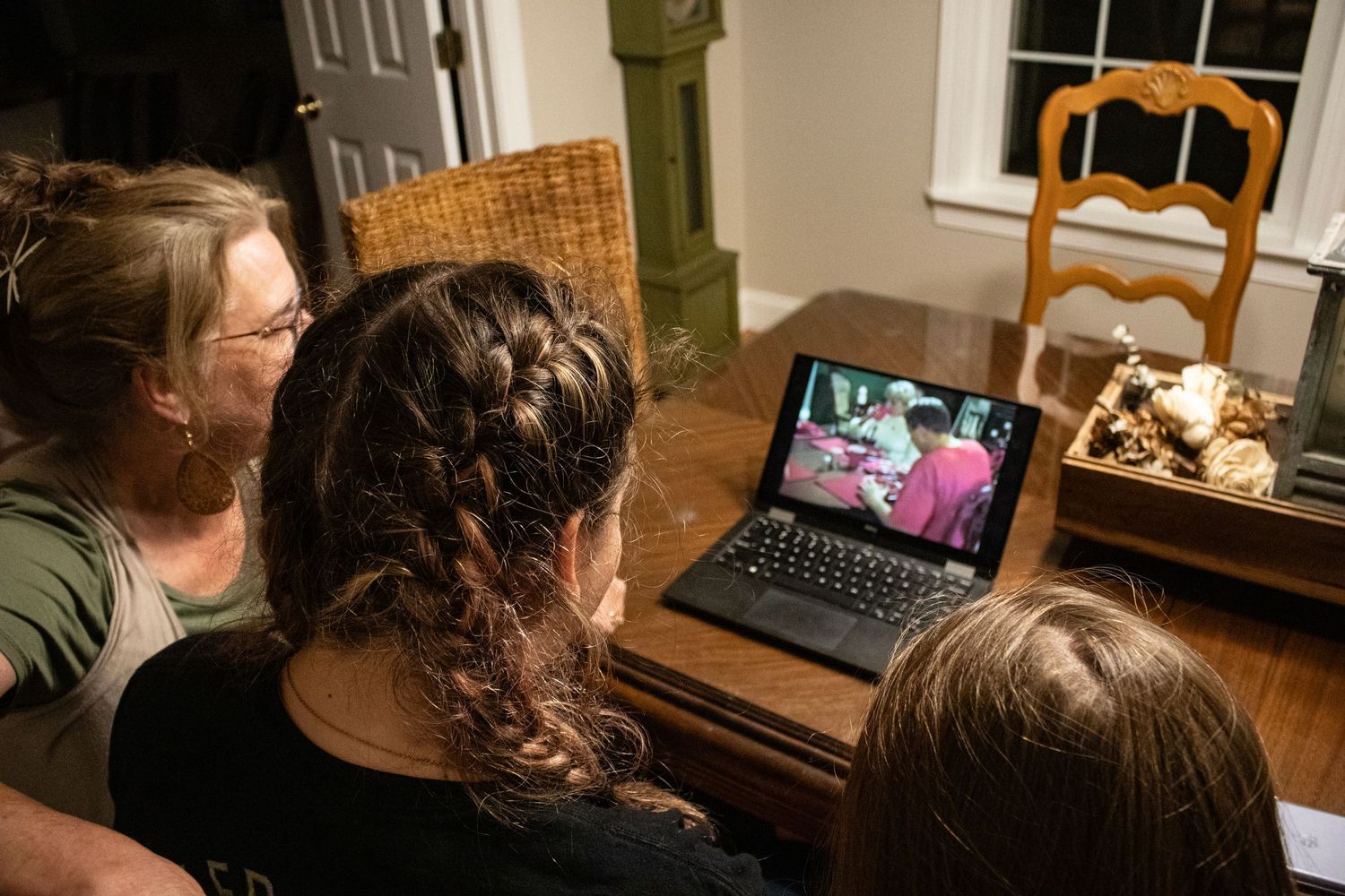 Mother with her 2 children watching her grandfather on video on a laptop on the kitchen table
