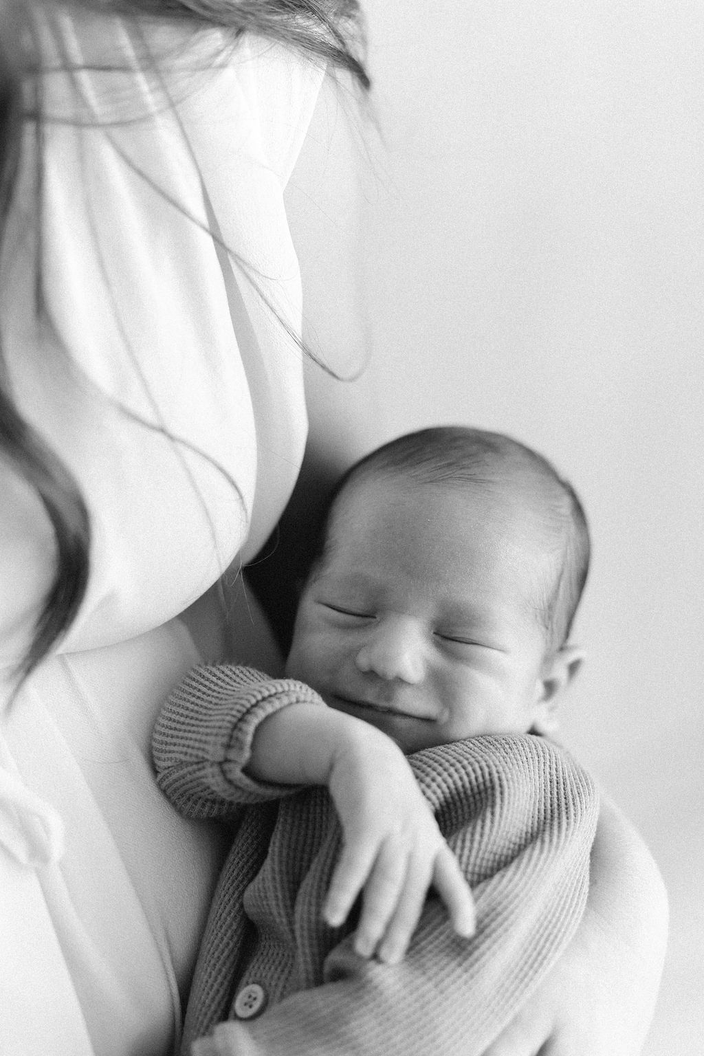A peaceful black and white image of a newborn baby sleeping in a knit sweater against white fabric.