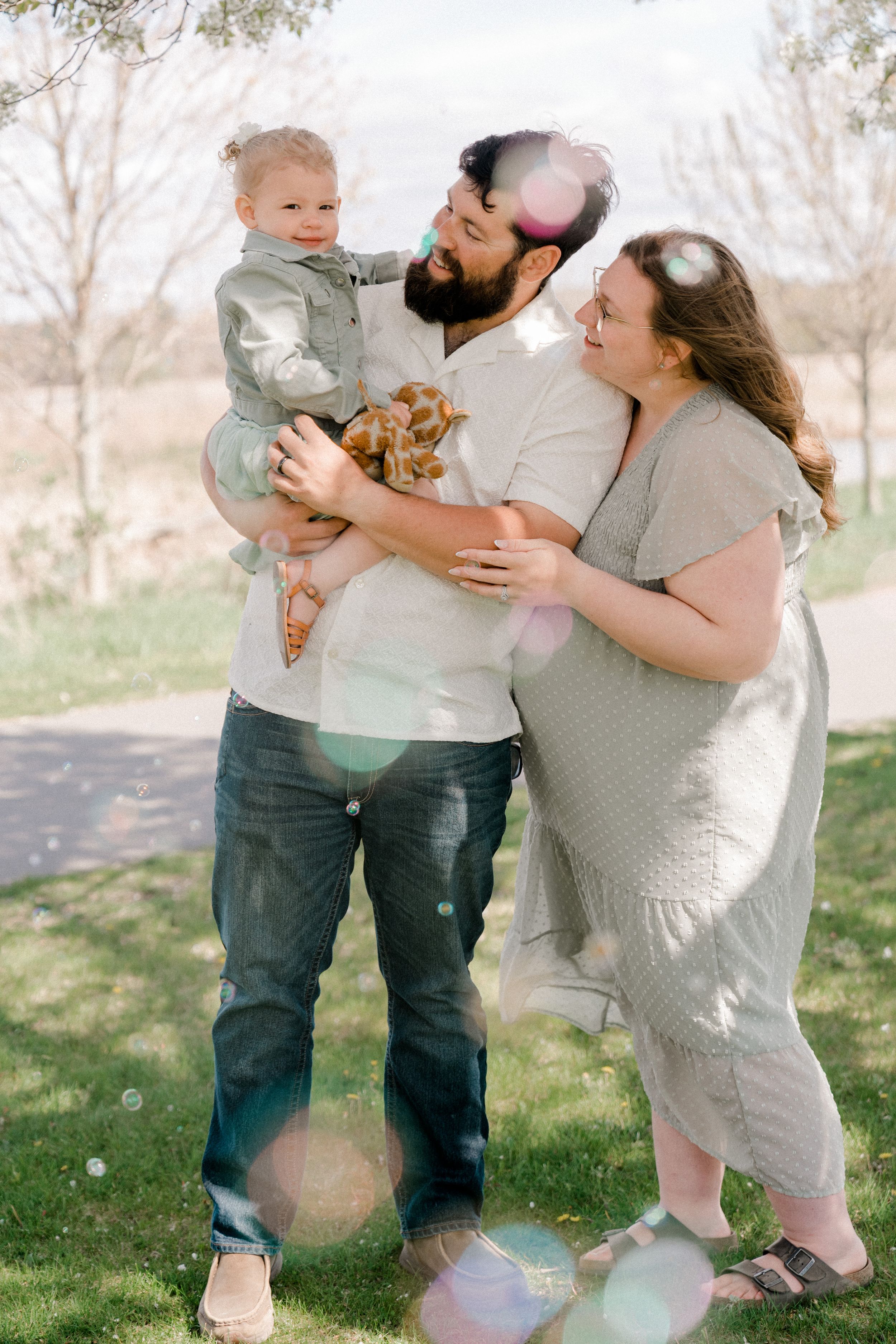 A family shares a tender moment together outdoors on a sunny spring day in a park setting.