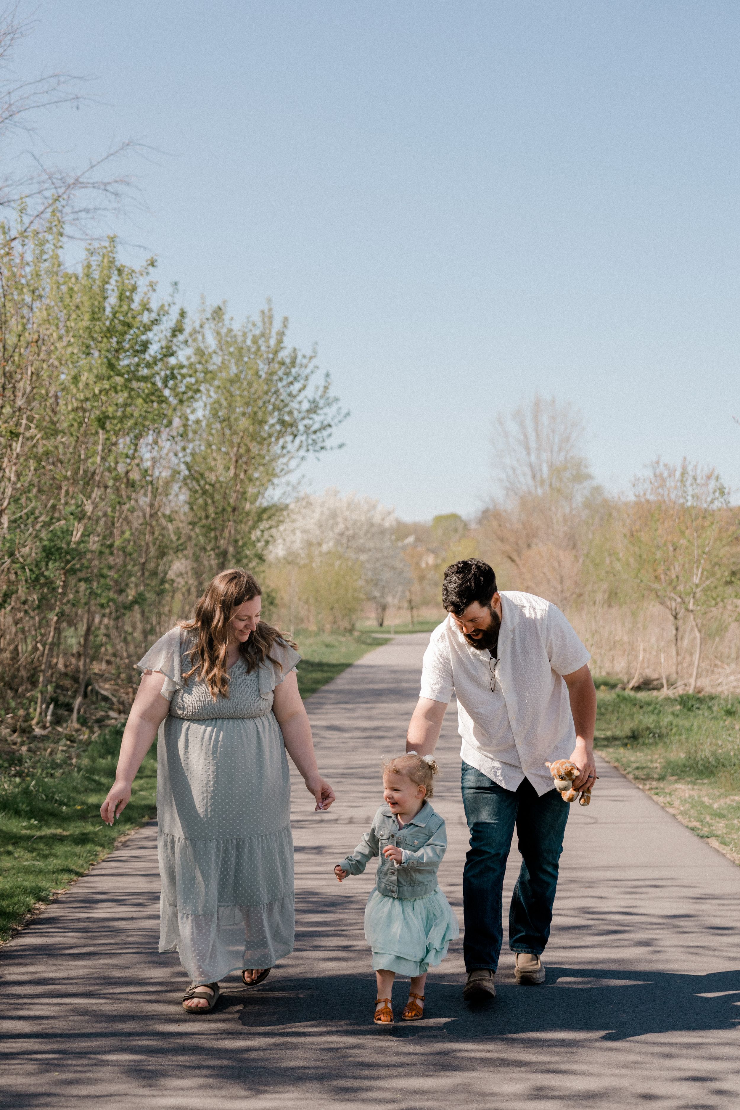 A family walks together on a paved path surrounded by spring greenery on a sunny afternoon.