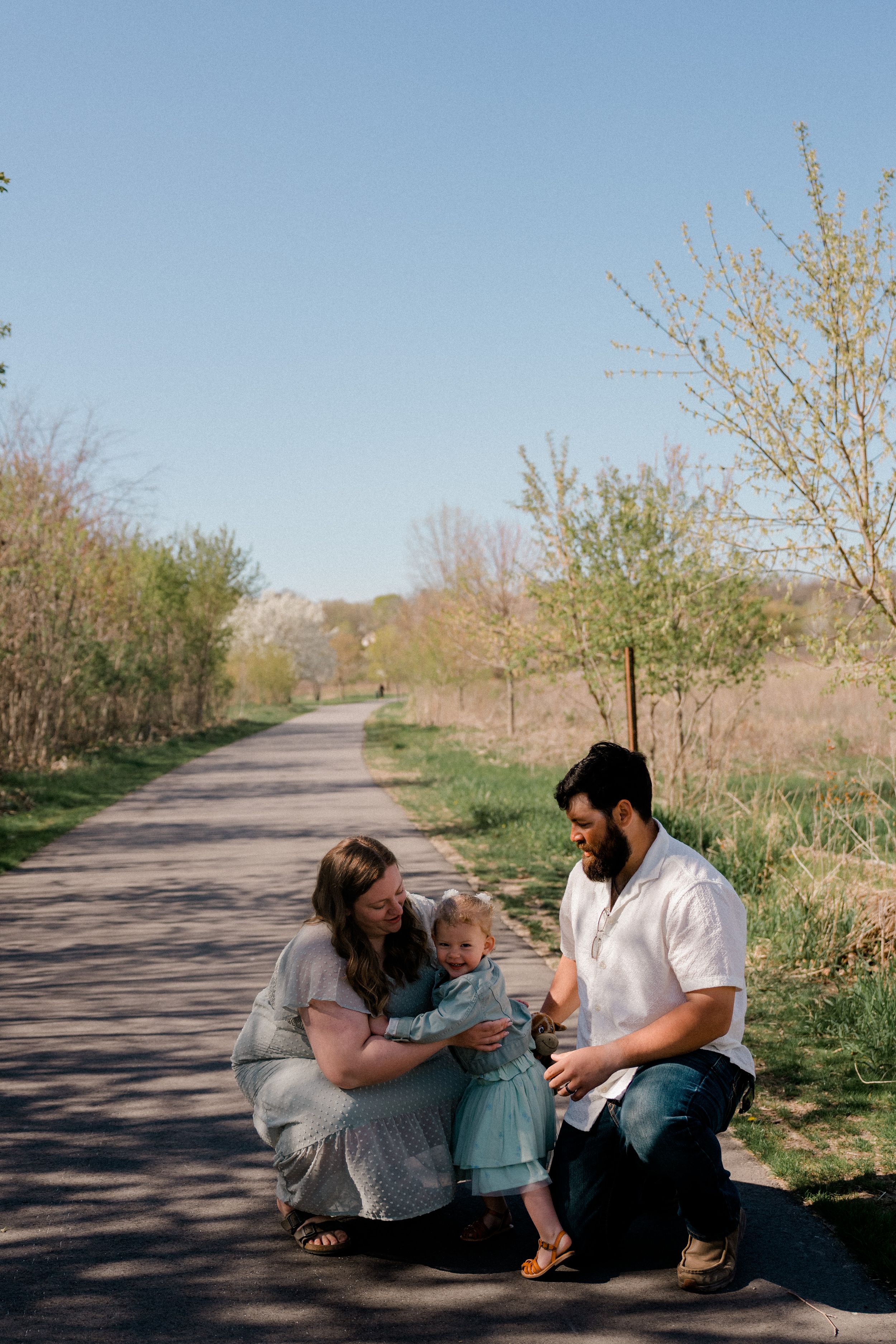 A family spending time together on a peaceful walking trail surrounded by spring budding trees and brush.