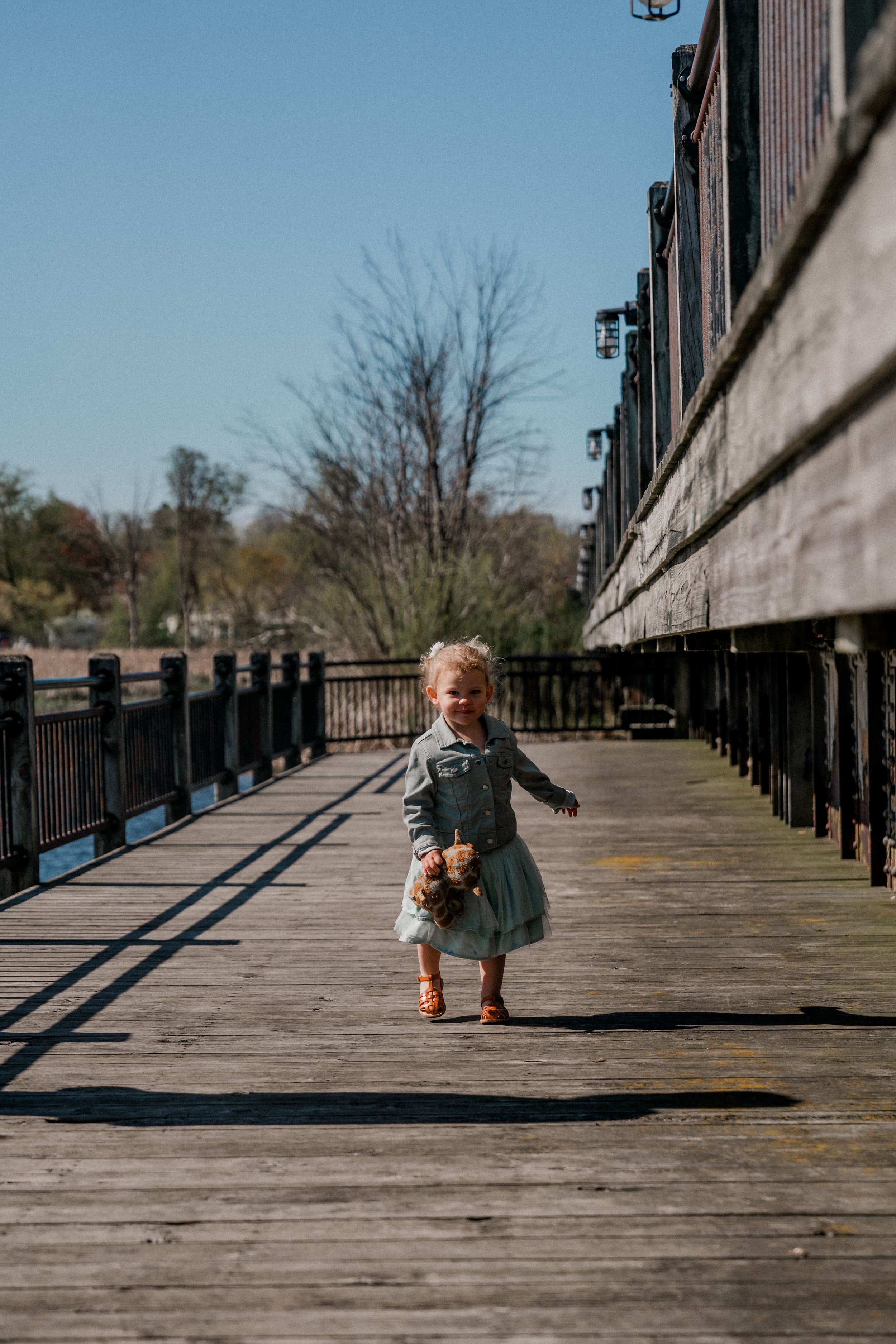 Small person in a dress joyfully jumping on a wooden pier or boardwalk on a bright sunny day.