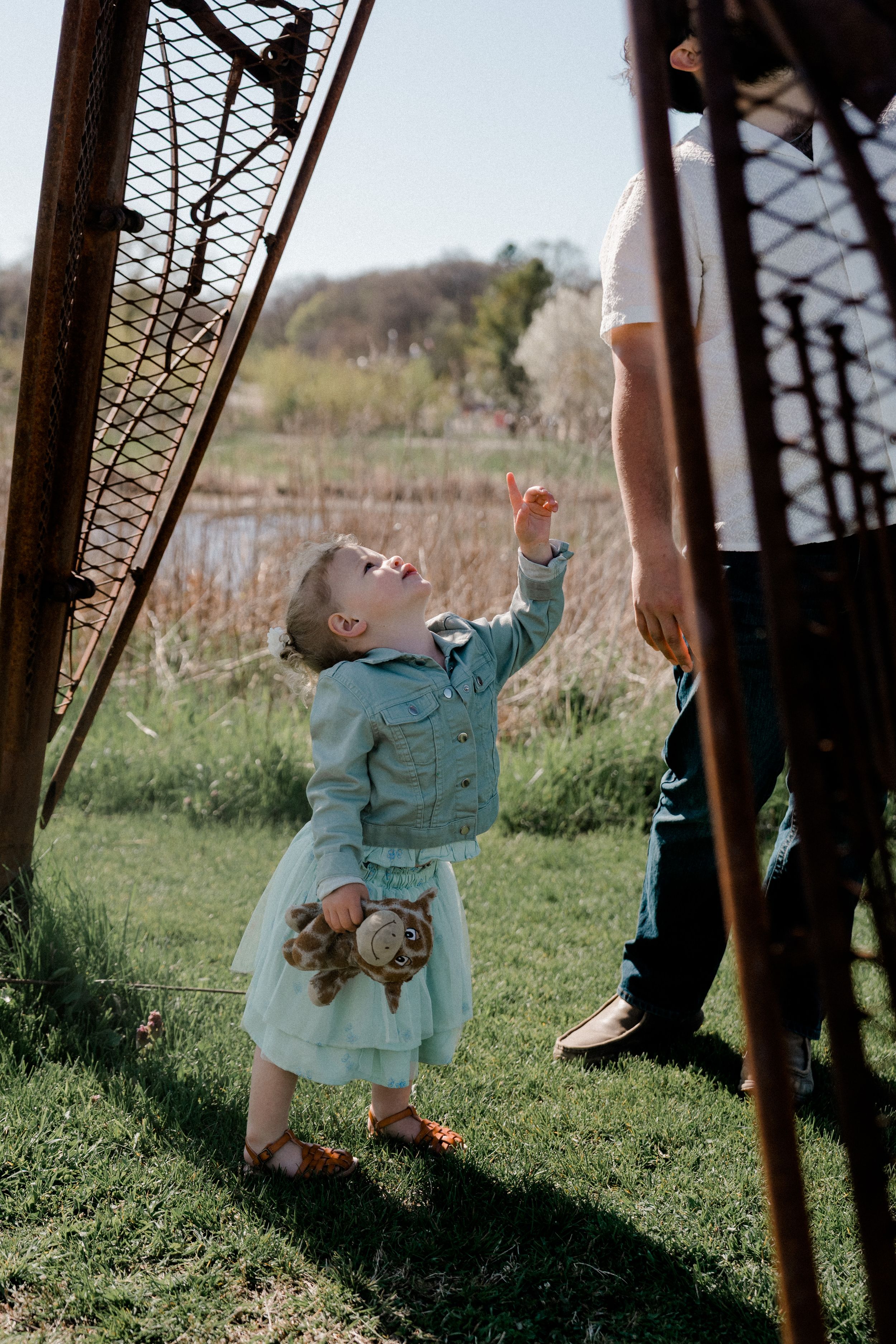 Four sequential outdoor photos show a child in a light blue outfit playing and dancing on grass near a metal structure.