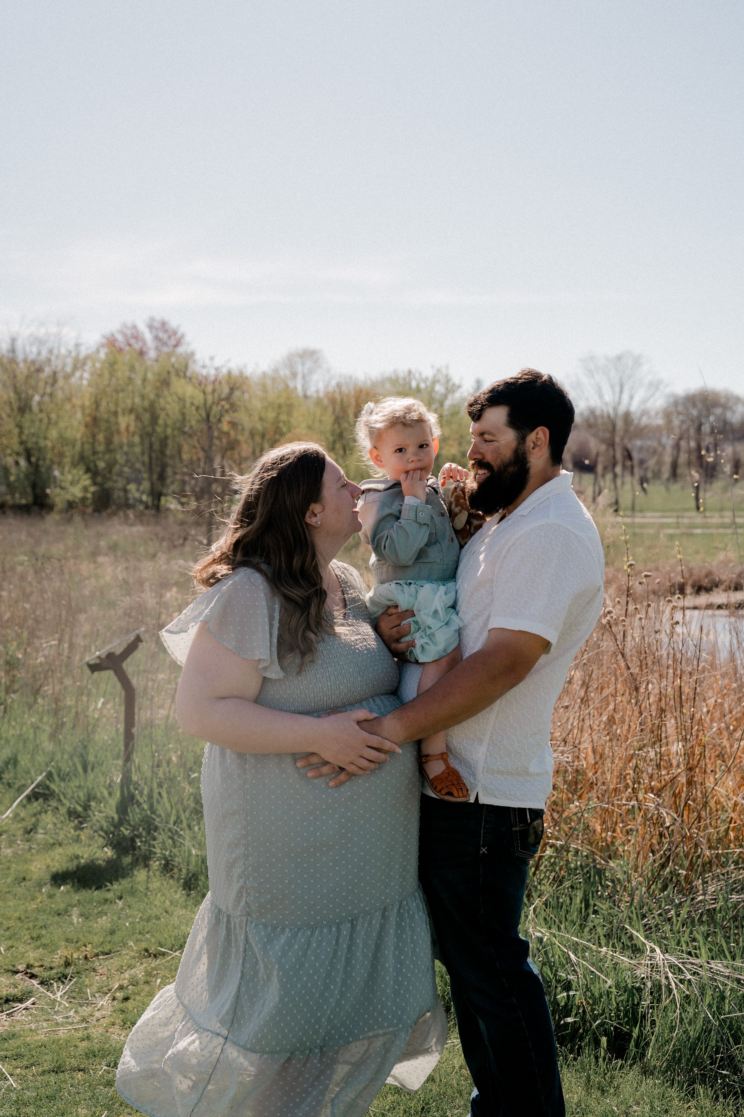 A family enjoys candid moments together in a springtime field with tall grass and natural lighting.
