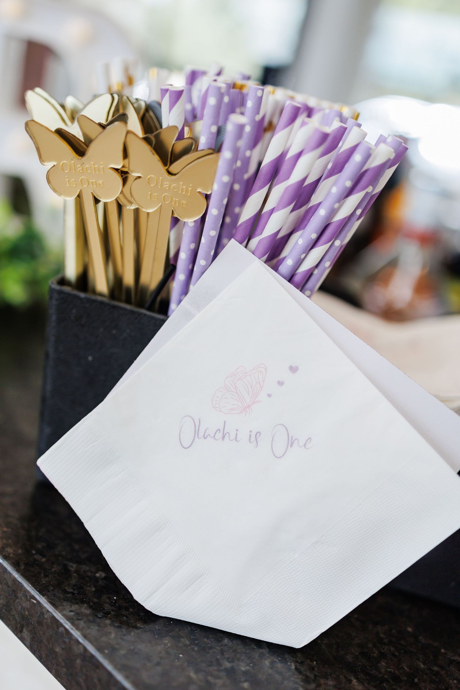 Gumball party favors decorated with lavender bows sit on a table at an elegant first birthday party place setting.