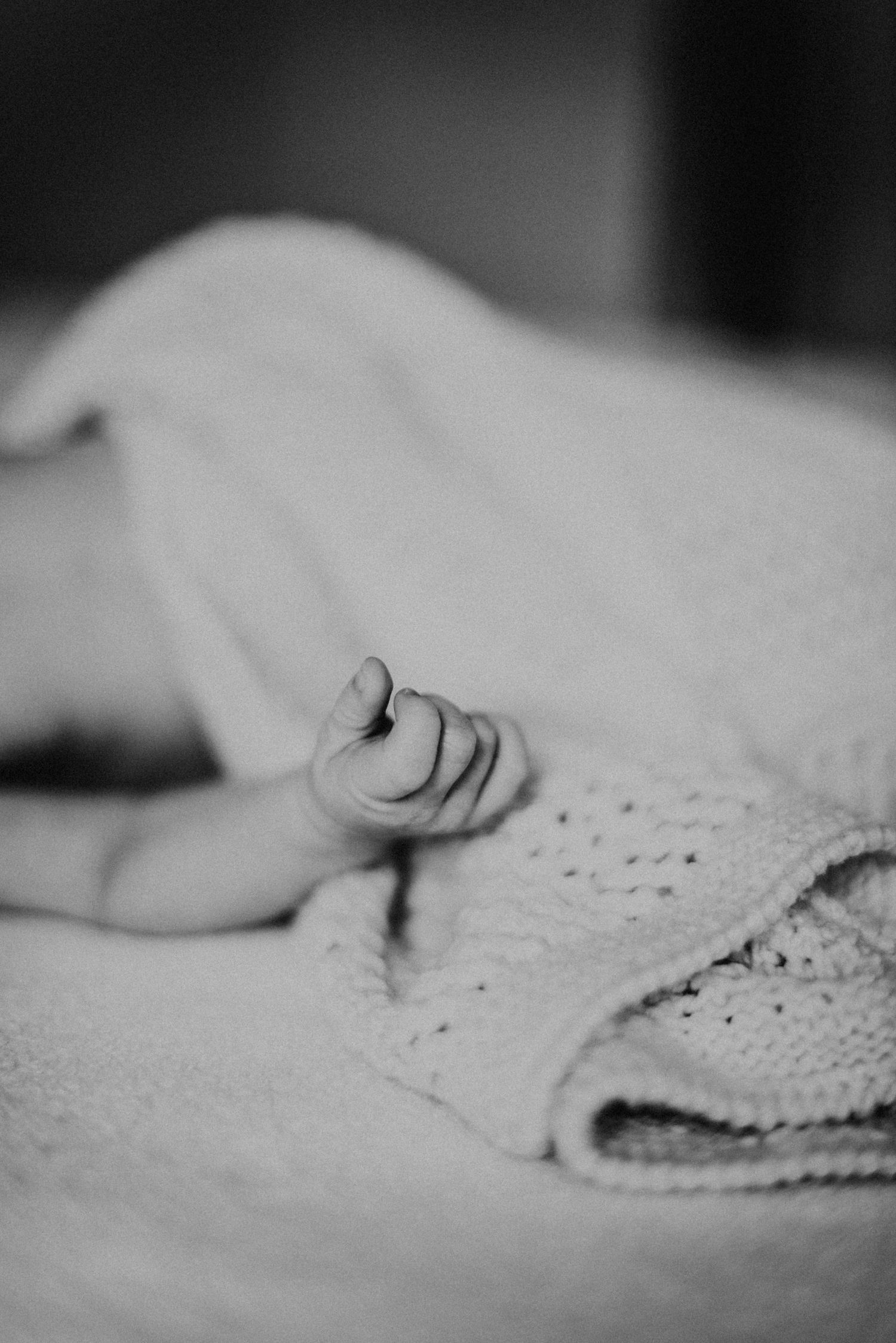 Schwarz-weiß-Foto eines schlafenden Babys, das unter einer gestrickten Decke liegt. Eine kleine Hand ragt hervor.