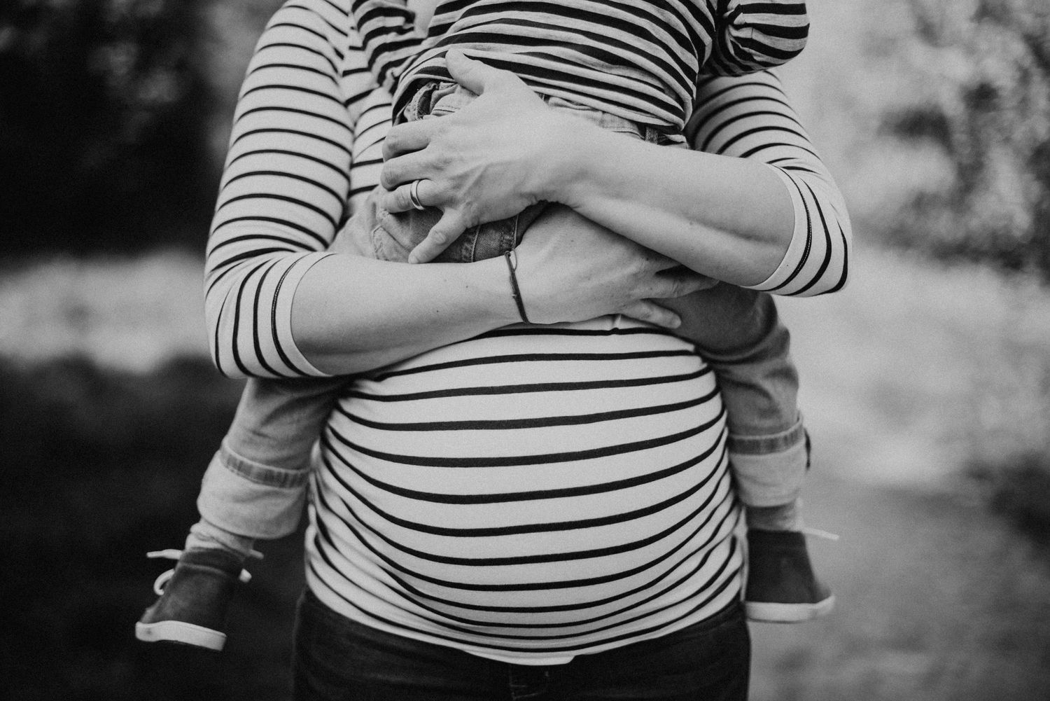 Eine Schwangere Frau hält ihr Kind vor der Brust. Ihr Babybauch ist in der Bildmitte. Schwartz-Weiss Portrait.