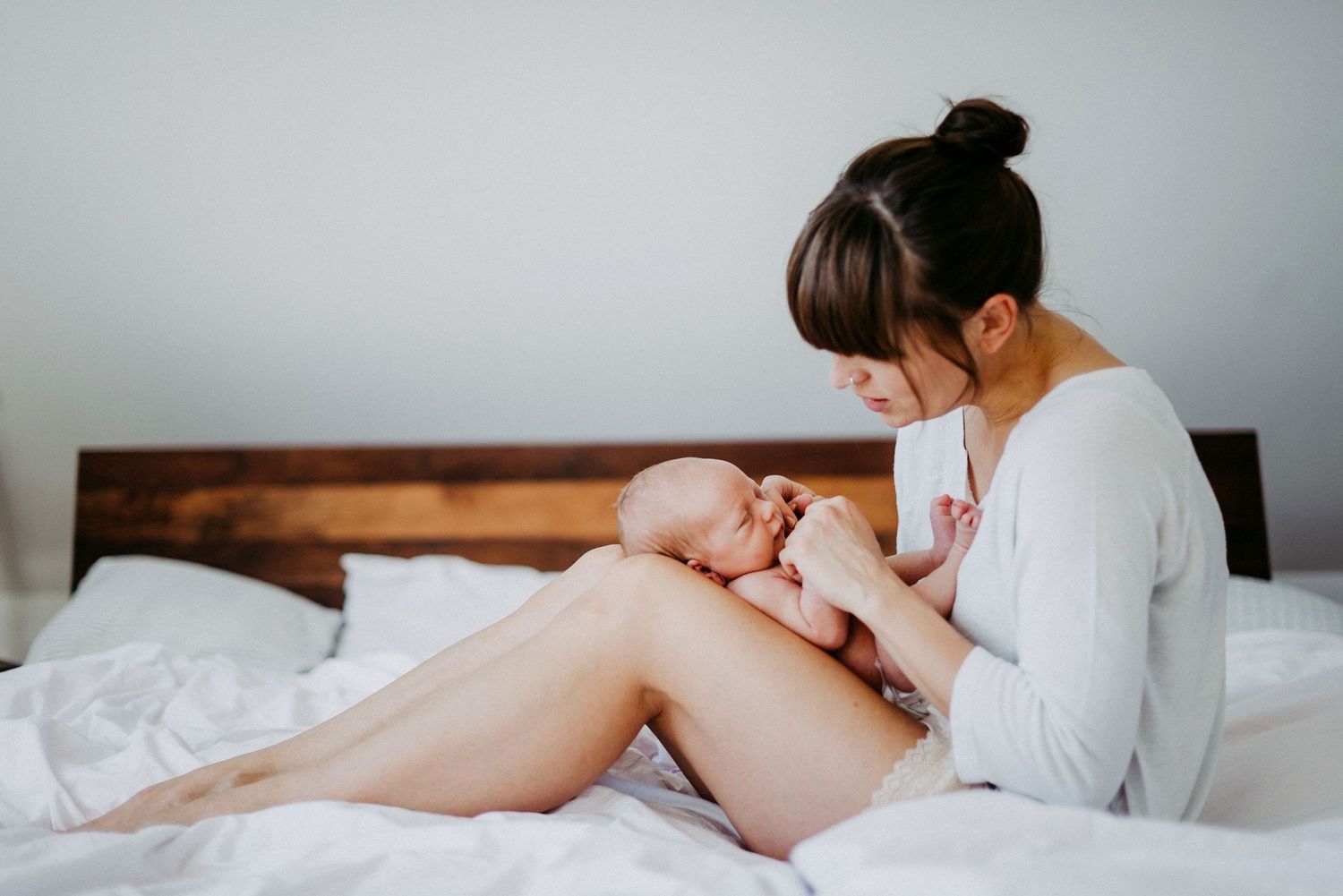 Frau sitzt auf einem Bett und hält ein Baby in den Armen. Sie schaut liebevoll auf das Baby, während sie es sanft hält.