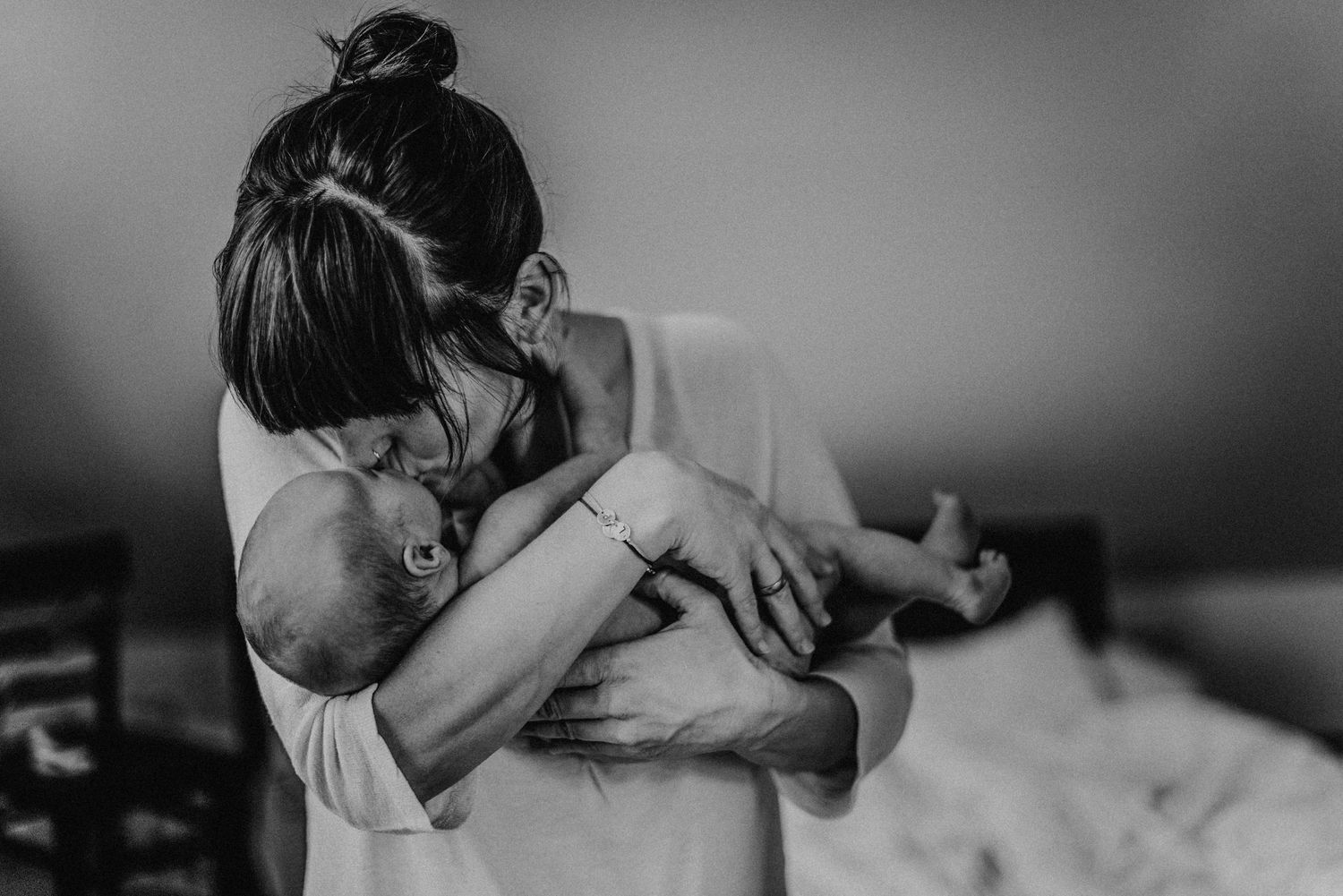 Eine Frau hält ein Baby liebevoll im Arm und küsst es auf die Stirn. Die Szene ist in Schwarz-Weiß gehalten.