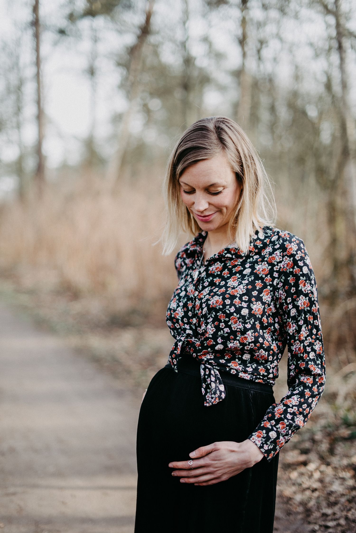 Eine schwangere Frau steht auf einem Weg in der Natur, sie hält zärtlich ihren Babybauch.