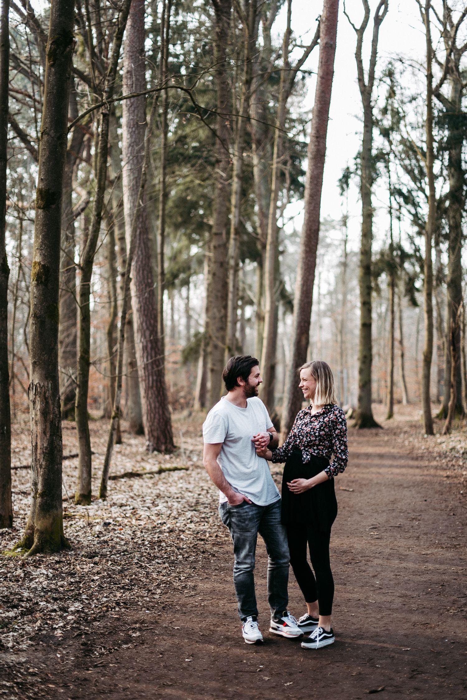 Ein Paar spaziert auf einem Waldweg. Der Mann trägt ein weißes T-Shirt, die Frau ein gemustertes Oberteil. Bäume im Hintergrund.