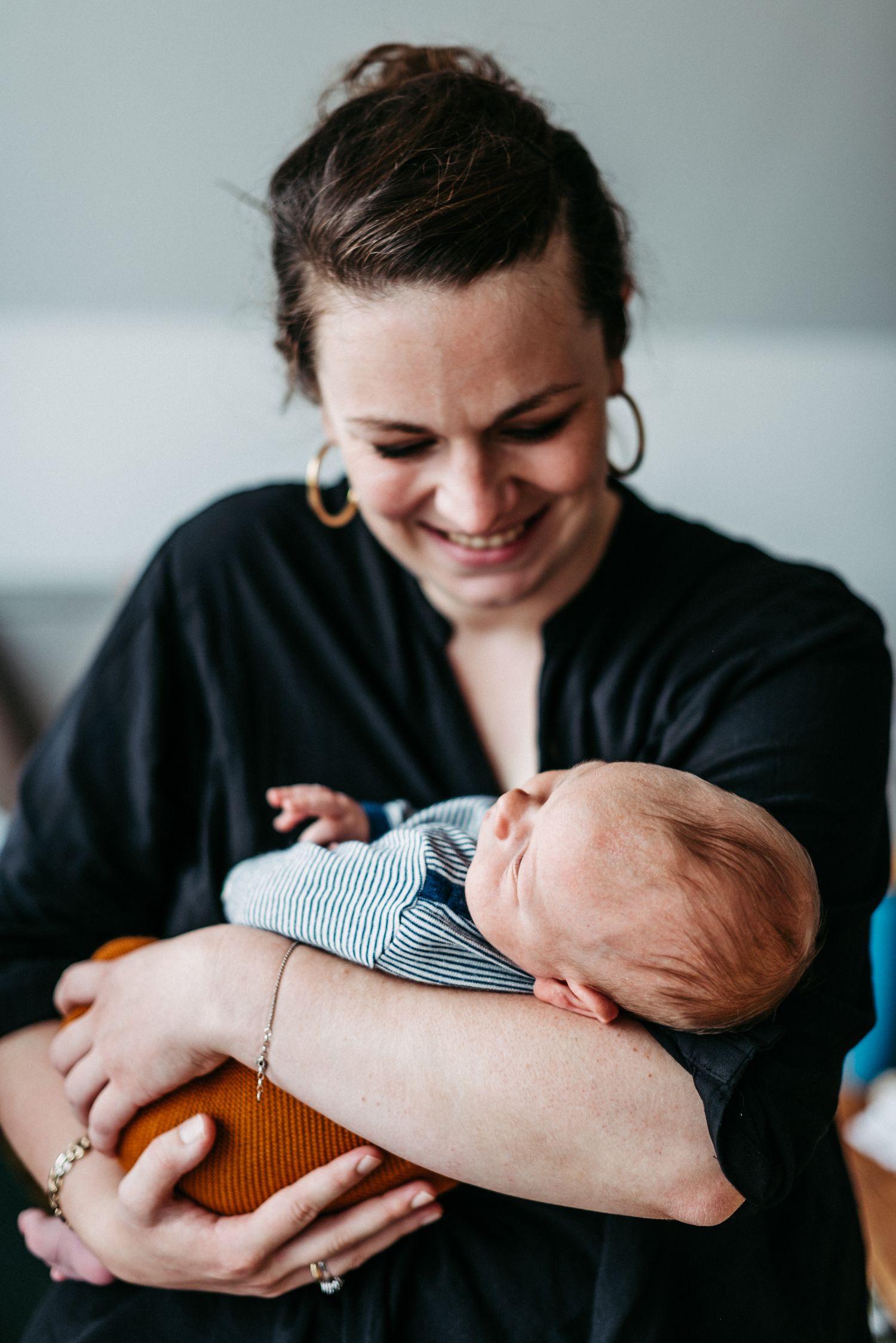 Frau in schwarzer Bluse hält lächelnd ein schlafendes Baby in den Armen. Die Szene wirkt warm und liebevoll.