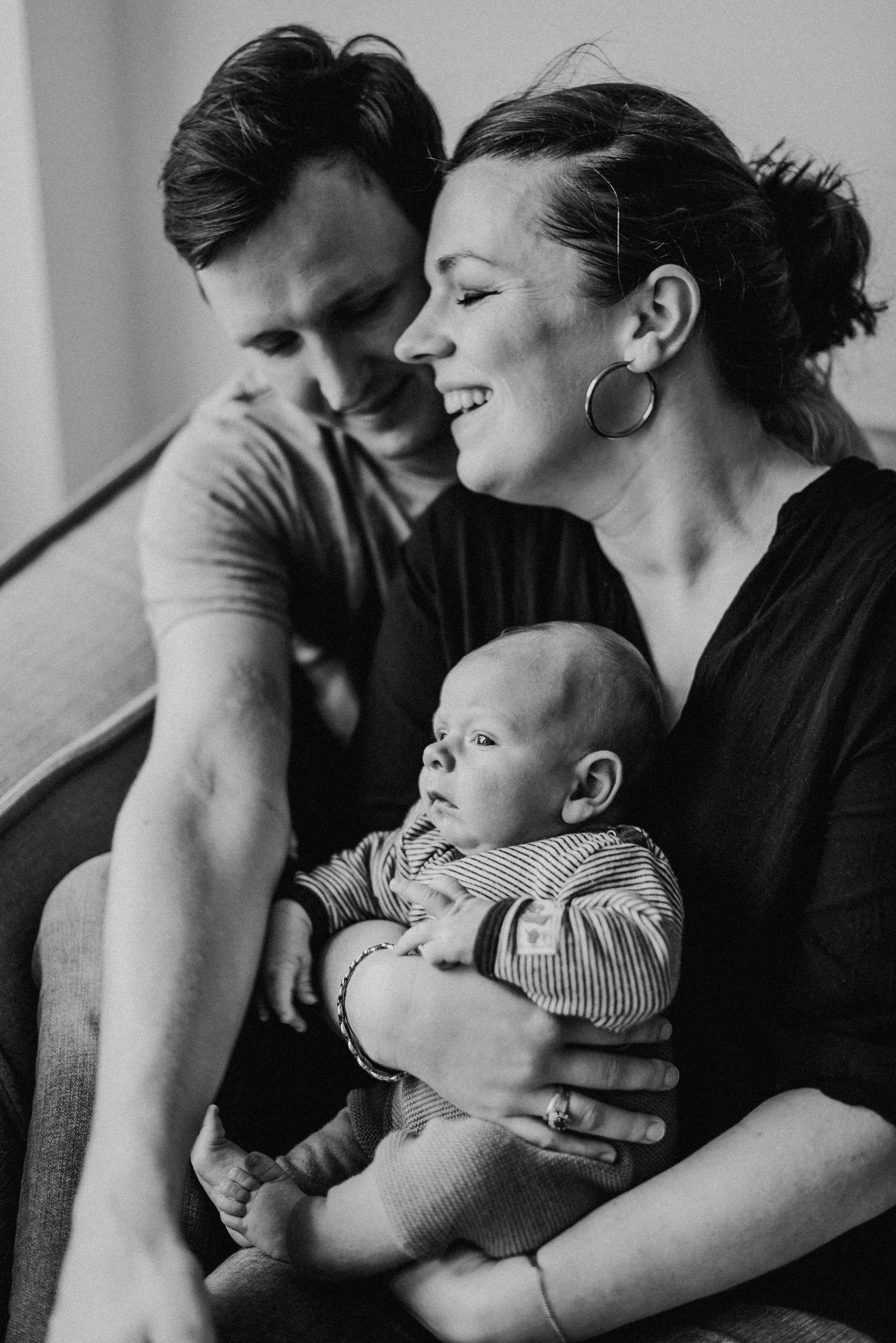 Ein lächelndes Paar sitzt auf einem Sofa und hält ein Baby im Arm. Die Szene strahlt Wärme und Familienglück aus.
