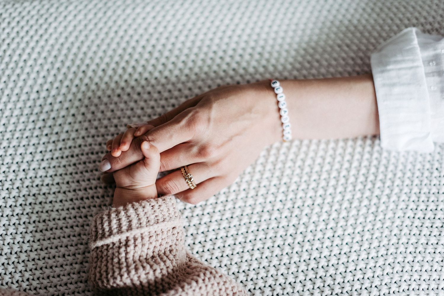 Baby hält liebevoll den Finger der Hand seiner Mutter.