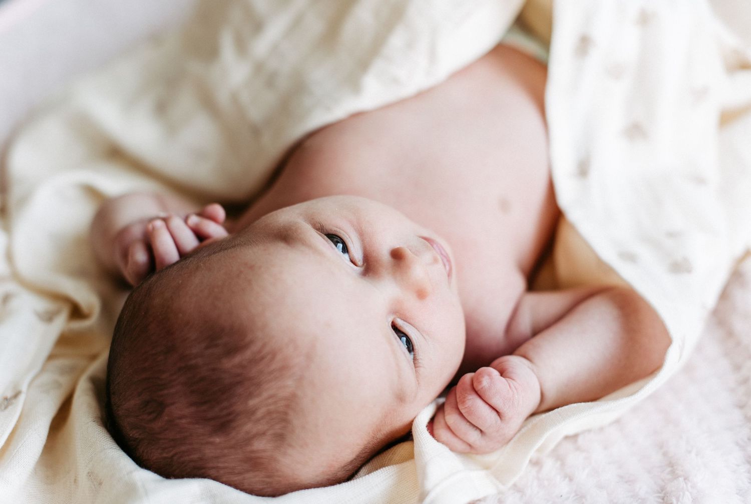 Ein kleines Baby liegt in ein weisses Tuch eingehüllt und schaut zur Seite.