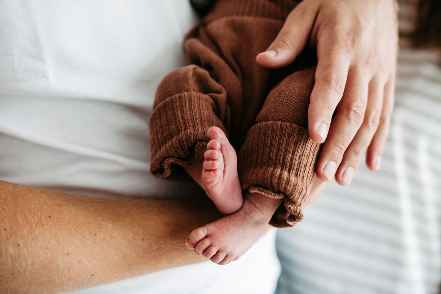 Babyfüße gucken aus eine branen Wollhose hervor. Das Baby liegt im Arm seiner Mutter.