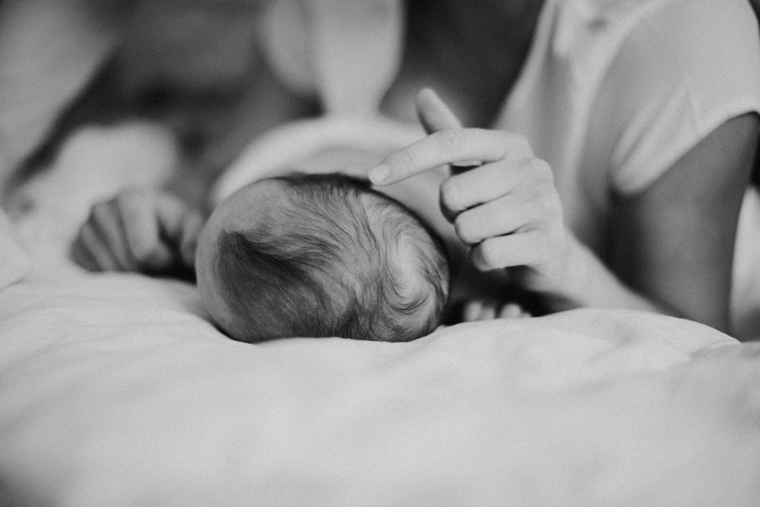 Eine Person hält sanft den Kopf eines schlafenden Babys, das auf einem weichen Bett liegt. Die Szene wirkt beruhigend und liebevoll.