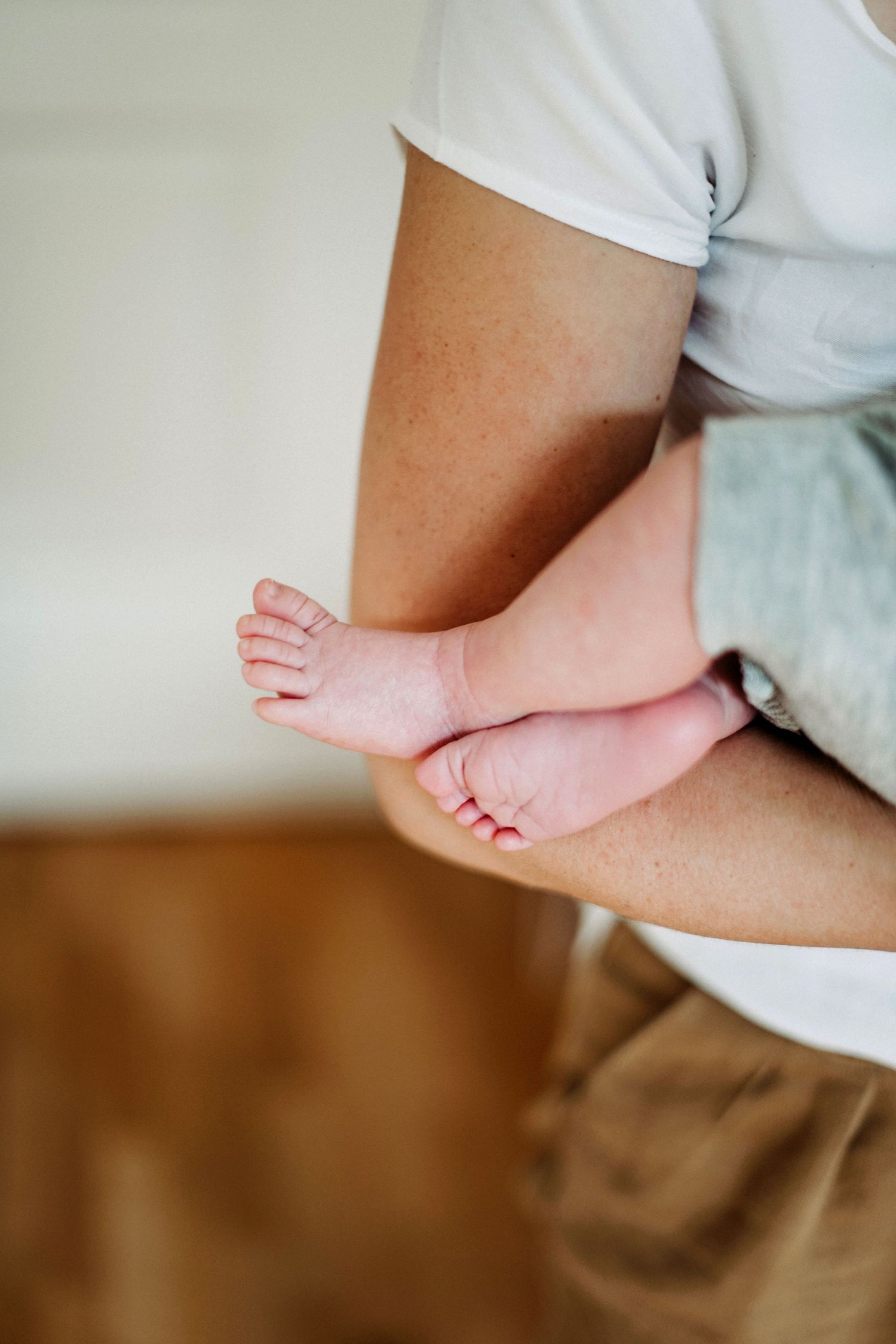 Eine Person hält ein Baby im Arm. Der Fokus liegt auf den kleinen Füßen des Babys, die aus einem grauen Strampler herausschauen.