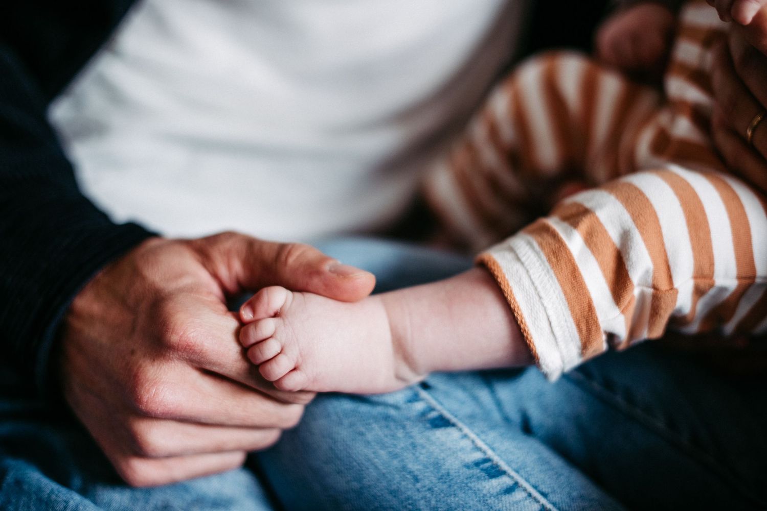 Papa hält den Babyfuß seiner Tochter in seiner Hand.