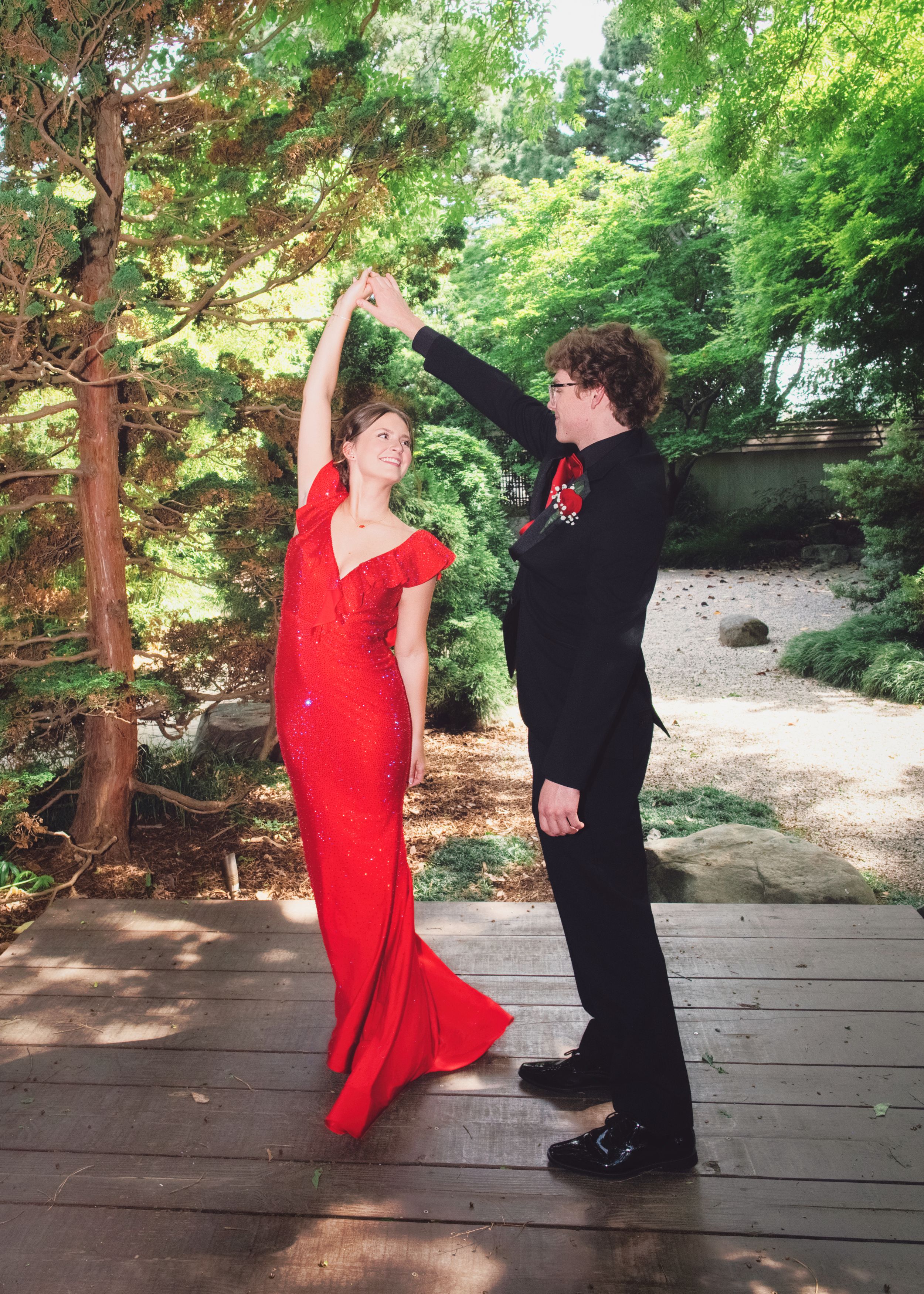 Couple in formal attire dancing on outdoor deck with woman in red gown and man in black suit.
