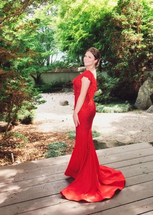 Elegant red mermaid gown with a dramatic train photographed on a wooden deck in a lush garden setting.