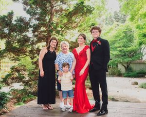A formal group photo outdoors with people dressed in formal attire including a red gown and black tuxedo.