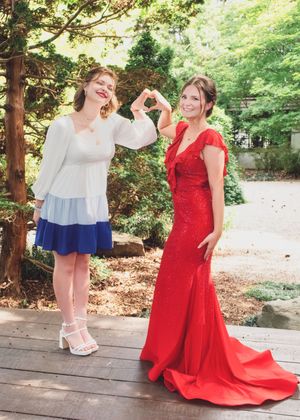 Two people sharing a fun moment outdoors, one wearing a white and navy outfit and another in a flowing red gown.