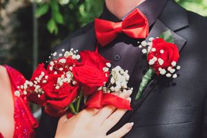 Close up of a formal black suit lapel with red roses, baby's breath flowers and a red bow tie.
