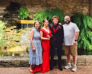 Four people pose together in formal and casual attire in front of a decorative stone water feature.