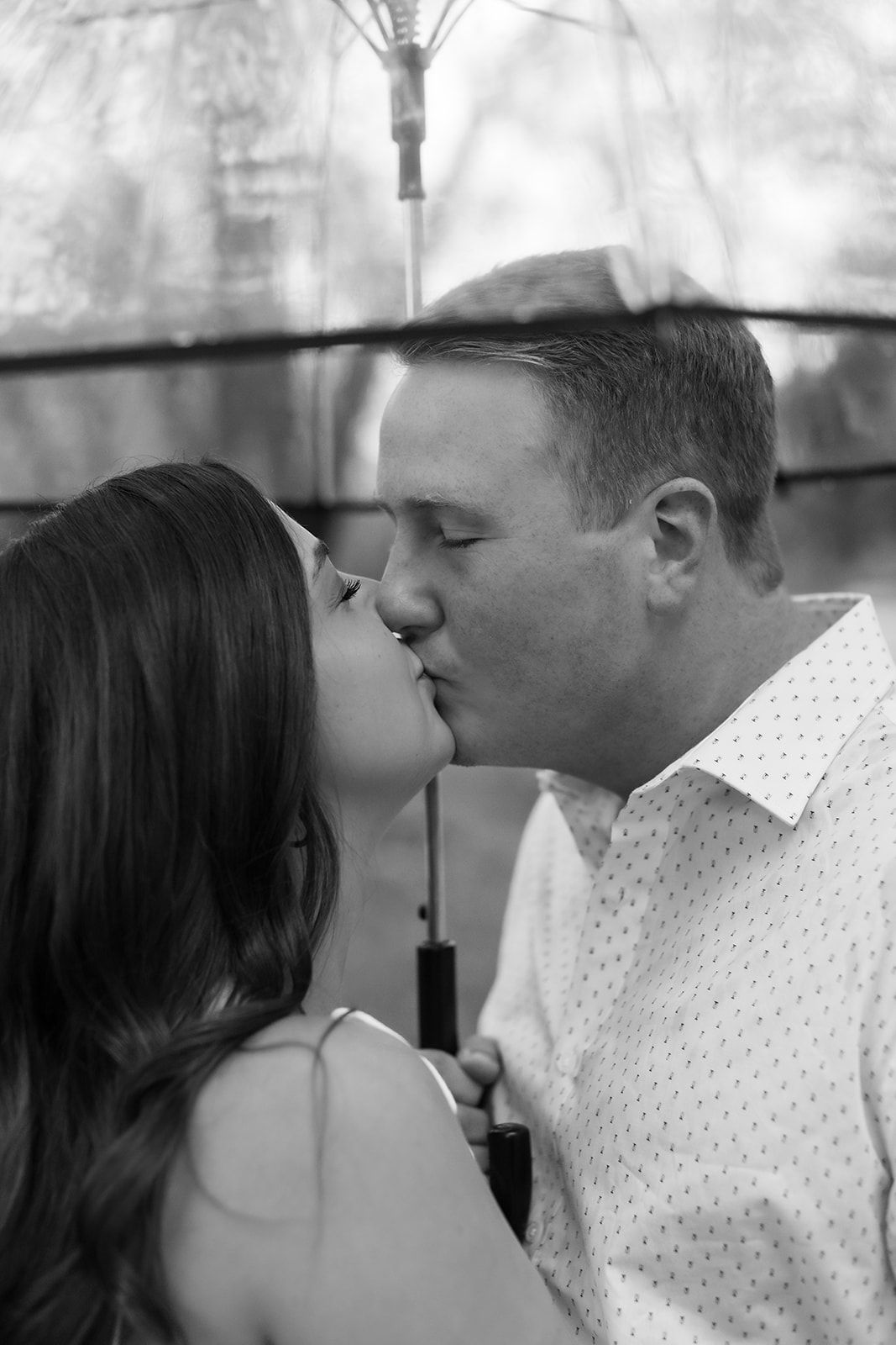 A romantic couple embraces and kisses on a wooden dock by the water on an overcast day.