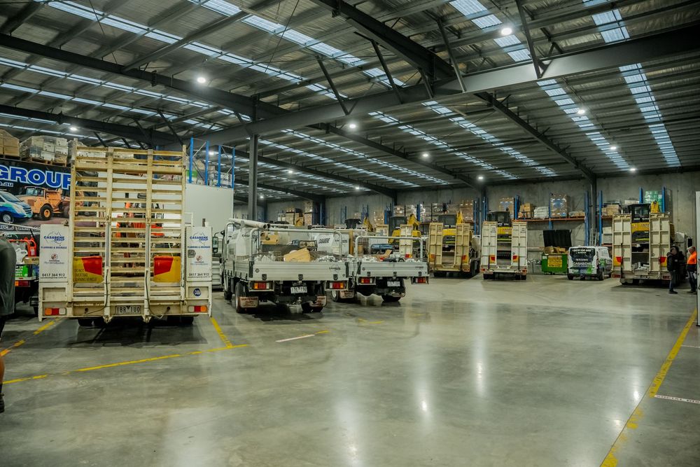 Industrial warehouse interior with loading docks, delivery trucks, and bright overhead lighting illuminating the concrete floor.