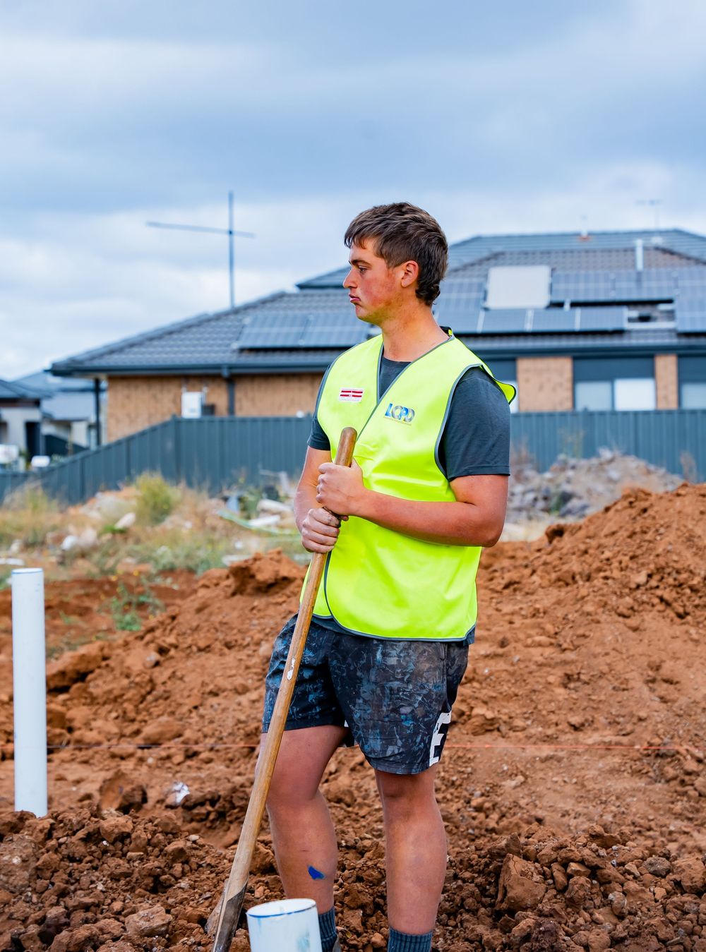 Construction worker in high-visibility vest uses measuring equipment on a mound of dirt at a building site.