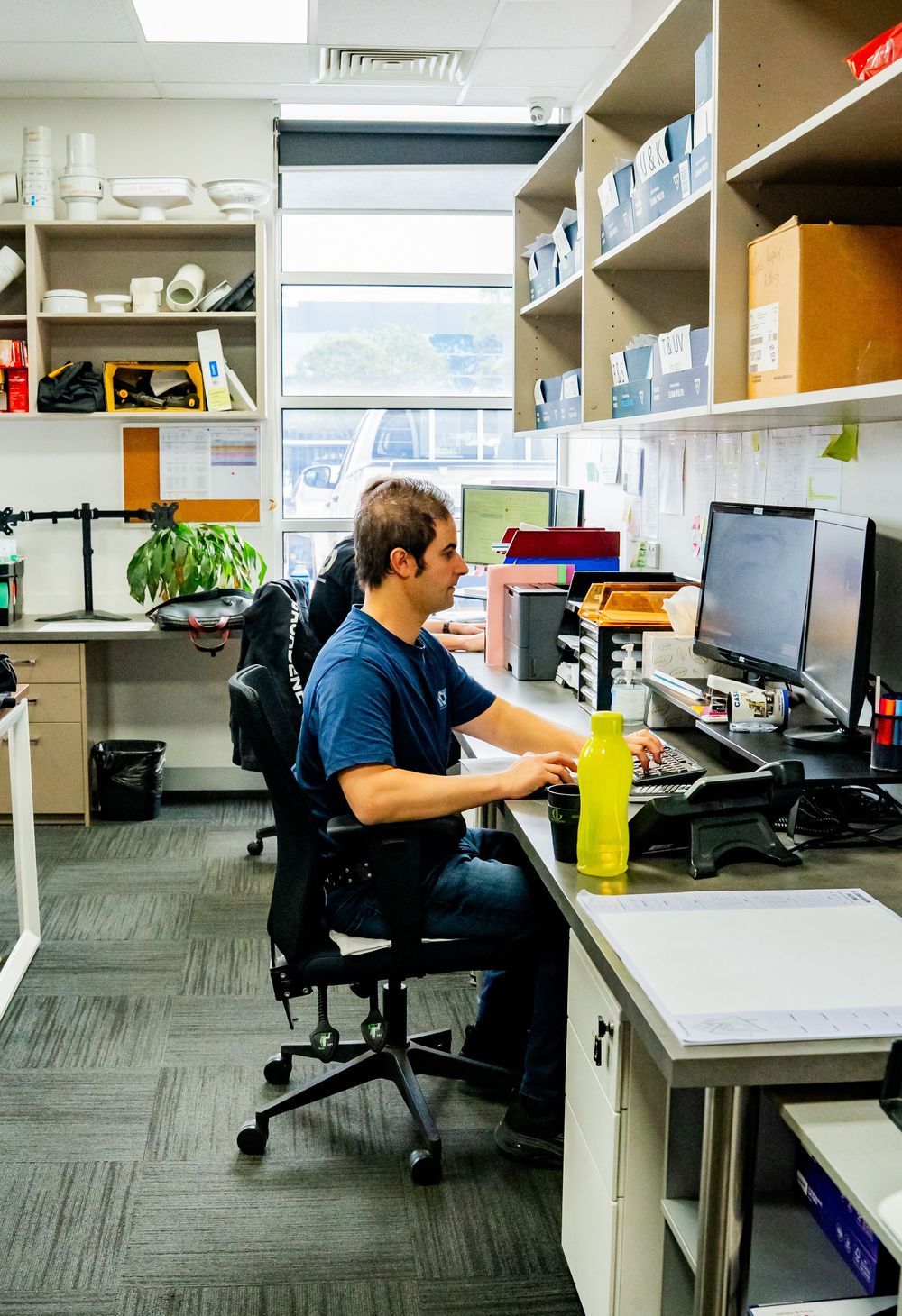 Workspace scene showing a row of desks with computers, chairs, and office equipment in a modern office environment.