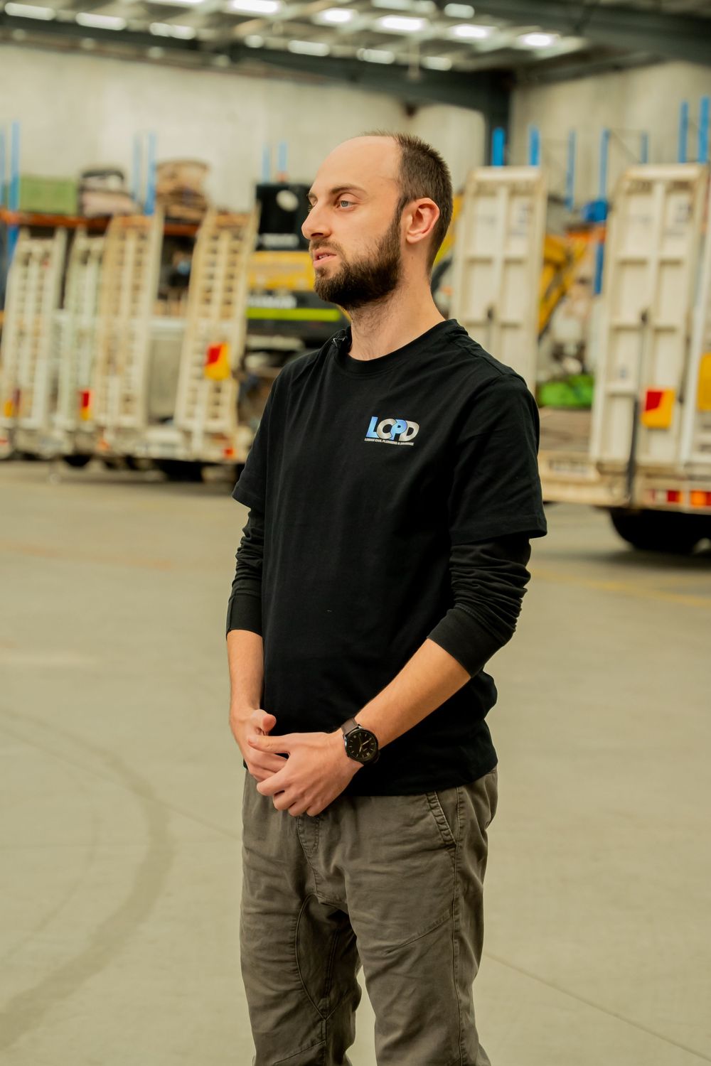 Person wearing black sweater and gray pants stands in front of delivery trucks in warehouse loading area.
